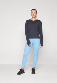 Top de manga larga azul marino con puños extendidos, combinado con leggings azul claro que cuentan con costuras laterales y una textura suave. Zapatillas deportivas negras.