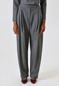 Grijze op maat gemaakte broek met plooien, gemaakt van een gestructureerde stof. Heeft een hoge taille en een wijde pijp, gecombineerd met bordeauxrode schoenen.
