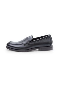 Mocasines de piel negra con un acabado suave, puntera redondeada y tacón bajo. Presenta una correa decorativa y detalles de costura en la parte frontal.