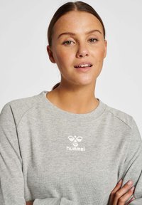 Grey sweatshirt with a round neckline and long sleeves. Features the white "hummel" logo on the chest. Made from soft, textured fabric.