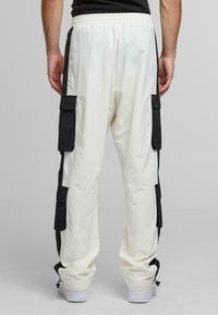 Cargo pants in white with black side panels; features side pockets, elastic waistband, and drawstring cuffs. Made from lightweight fabric.