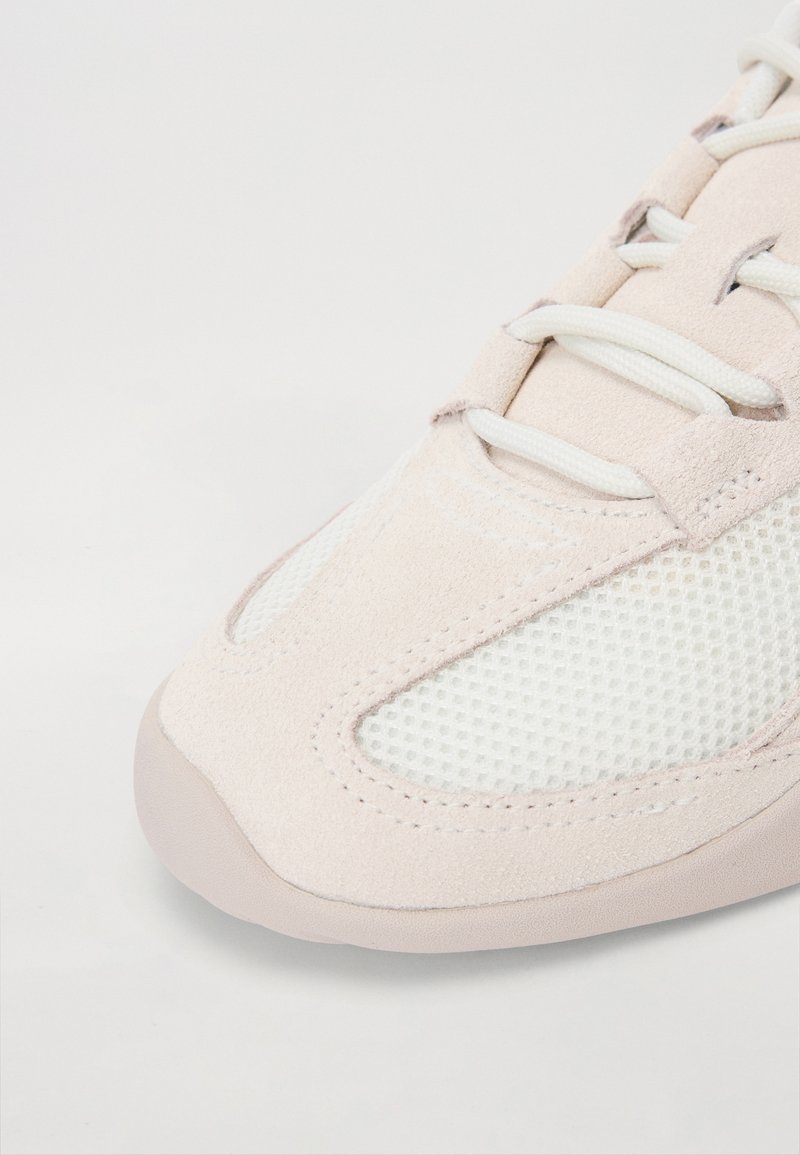 Baskets rose clair avec des panneaux en daim et en maille, bout rond et semelle en caoutchouc texturée avec des lacets blancs contrastés.