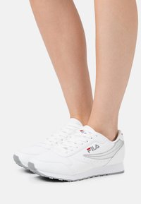 Baskets blanches avec une tige en cuir lisse, des accents gris, des détails perforés et un bout rond. Lacets, col rembourré et semelle en caoutchouc visibles.