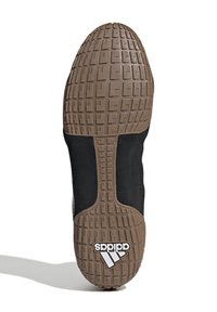 Sula till sko med brun strukturerad tugg och svart ovandel, med vit Adidas-logga nära hälen.