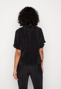 Zwarte geplooide top met korte ruches mouwen en een zachte kraag. Kenmerkt zich door een relaxte pasvorm en een gestructureerde stof.