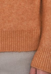 Oranžinė megzta suknelė su raštuotu apdaila ir rankogaliais. Minkšta tekstūra, prigludęs dizainas. Derinama su šviesiai pilku raštuotu audiniu apačioje.