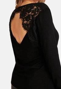 Sort langærmet top med en dyb V-ryg, der har detaljeret blonder på skuldrene og en glat, tætsiddende struktur.
