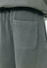 Grå sweatpants med en sidelomme i rektangulær form og syede kanter, lavet af blød, tekstureret stof. Elastisk talje synlig.