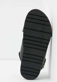 Semelle de sandale noire, avec du caoutchouc texturé et des rayures horizontales en relief, taille indiquée comme 37, conception robuste et lignes épurées.