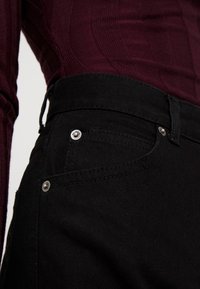 Svarta denimjeans med en slät textur, femfickorsdesign, metallbeslag och en figursydd midja.