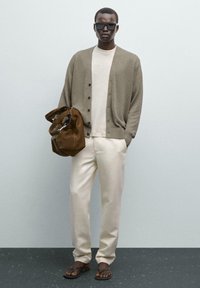 Beige Cardigan, cremfarbene Bluse, helle Hose, dunkle Sandalen; hält eine braune Wildledertasche; glatter Stoff, lockere Passform, minimalistisches Design.