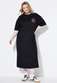 Czarna, oversize sukienka T-shirt z różowym napisem "Love" na klatce piersiowej, w połączeniu z białymi trampkami i różowymi skarpetkami w paski. Gładki materiał bawełniany.