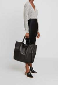 Große schwarze Leder-Tote mit zwei Griffen und strukturiertem Finish, ergänzt durch ein stilvolles, glattes Schwarz-Weiß-Outfit und spitz zulaufende Mules.