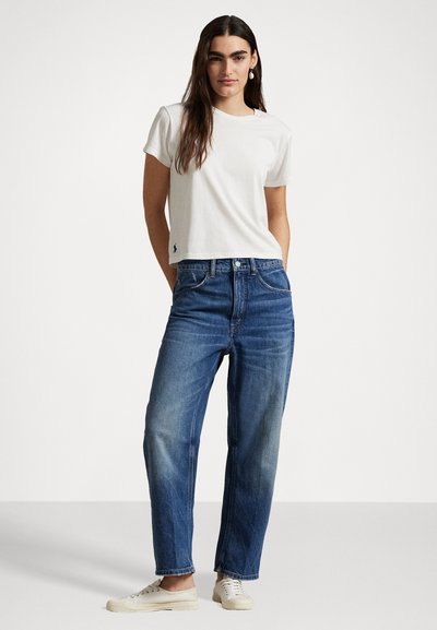 White cotton T-shirt with short sleeves, blue denim jeans with a straight fit, and white sneakers, set against a plain background.