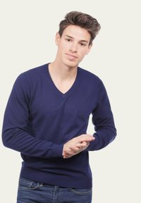 Pull en v bleu marine, coupe ajustée, confectionné dans un tissu doux avec des poignets et un ourlet côtelés. Porté sur un jean en denim sombre.