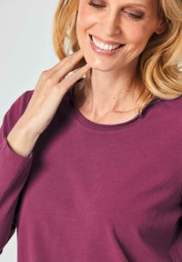 Paarse langärmige shirt met een ronde halslijn. De stof lijkt zacht en heeft een gladde textuur zonder opvallende patronen of details.