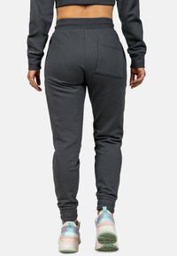 Graue Jogginghose mit elastischem Bund, Rippbündchen und einer Gesäßtasche, kombiniert mit hellen Sportschuhen.