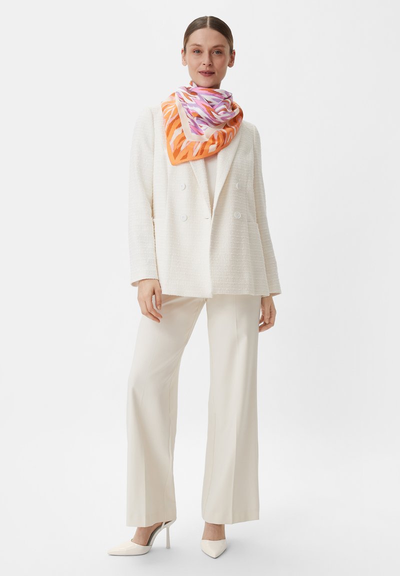 Biała, teksturowana marynarka na jasnej koszulce na ramiączkach, zestawiona z kremowymi spodniami o szerokich nogawkach i kolorowym jedwabnym szalem w pomarańczowe i różowe wzory.