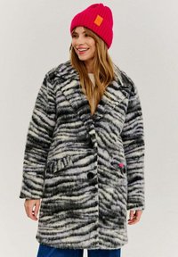 Dlhý kabát s čierno-bielym zebrovým vzorom, vyrobený z mäkkého materiálu. Navrhnutý s vypchávkovaným golierom, gombíkmi a bočnými vreckami.