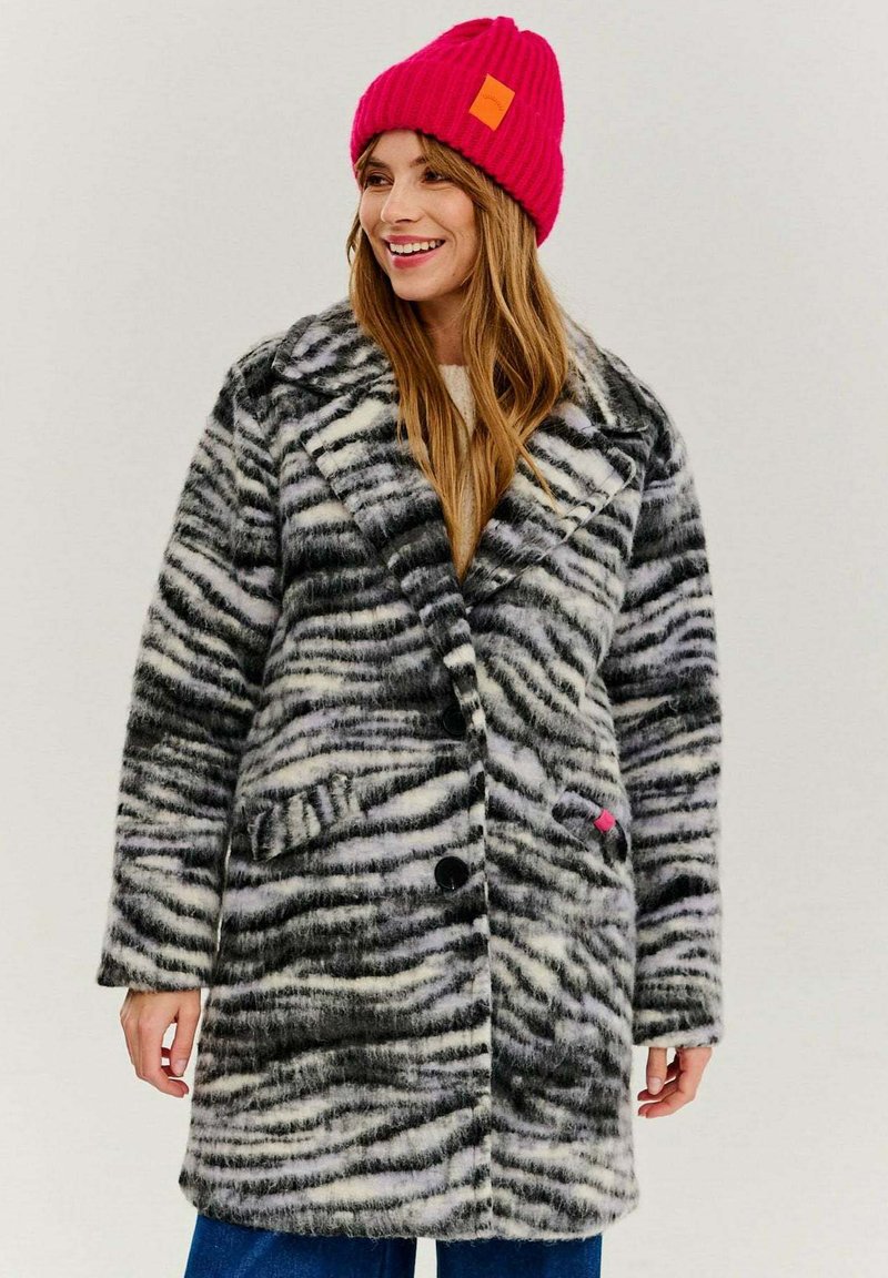 Dlhý kabát s čierno-bielym zebrovým vzorom, vyrobený z mäkkého materiálu. Navrhnutý s vypchávkovaným golierom, gombíkmi a bočnými vreckami.