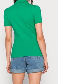 Polo vert à manches courtes, texture lisse et col classique, associé à un short en denim retroussé de couleur clair.