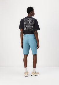 Black graphic t-shirt with white print, paired with light blue shorts. Shorts have a smooth texture and back pockets. Beige sneakers with white socks.
