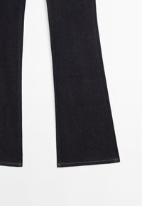 Dunkelblaue, ausgestellte Denim-Hosen mit glatter Textur, die einen sauberen Abschluss und kontrastierende Nähten am Saum aufweisen.