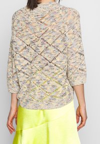 Pull léger multicolore en maille avec un motif losange ajouré et des manches trois quarts, associé à une jupe jaune vif.