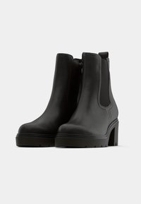 Stivali alla caviglia neri in pelle liscia, con alto tacco a blocco, cerniera laterale e pannelli elasticizzati per una facile calzata.