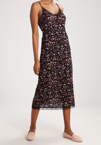 Schwarzes Blumenkleid mit dünnen Trägern, Spitzenbesatz und einem knielangen Saum. Es hat ein kleines Blumenmuster in Rosa- und Weißtönen.