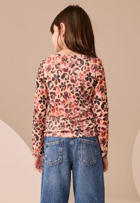 Leopard-print long-sleeve shirt in soft fabric, featuring orange, black, and pink tones. Paired with blue denim jeans, showcasing back pockets.