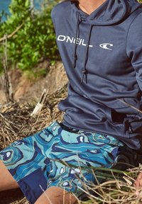 Marinblå hoodie med O'Neill-logotyp och blå mönstrade badshorts med abstrakta former och en mörkare accentpanel. Texturerad tyg, avslappnad passform.