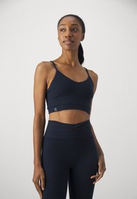 Soutien-gorge de sport en maille côtelée marine avec bretelles réglables et une large bande, associé à un legging côtelé taille haute avec un détail de ruché à l'avant.