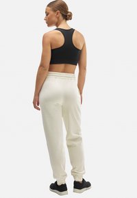 Sujetador deportivo negro con diseño de espalda nadadora, combinado con pantalones de chándal blancos que tienen una cinturilla elástica y zapatillas negras. Sencillo y funcional.