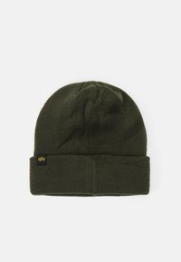 Tmavozelená pletená čiapka s prehnutým okrajom, na ktorej je malá čierna nálepka so žltým emblémom. Mäkkučká textúra a rebrovaný dizajn.