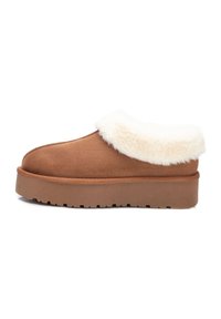 Zapato mocasín de ante marrón con un cuello de pelo sintético blanco, que presenta una suela de plataforma gruesa y una textura en la suela para mayor agarre.