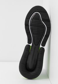 Svart atletisk sko sula med texturerat grepp, vita accenter och en grön sektion. Har varierande mönster på sulan och är tillverkad av gummimaterial.