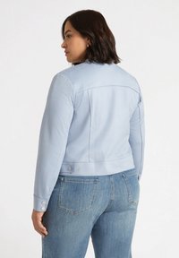 Chaqueta corta de color azul claro con mangas largas, que presenta una textura suave, detalles de botones en los puños y un diseño sencillo.