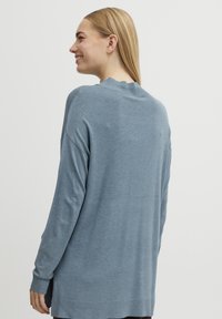Pull léger bleu, à manches longues, avec un col rond, des poignets côtelés et une coupe décontractée. Texture douce, légèrement plus long au dos.