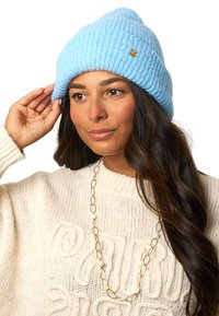 Niebieska czapka typu beanie z prążkowanego dzianiny, wykonana z miękkiej włóczki, z małym złotym logo. Projekt ma zgięty mankiet i luźną górę.