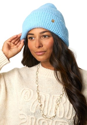 Blauer gerippter Strickbeanie aus weichem Garn, mit einem kleinen goldenen Logo-Akzent. Das Design hat einen umgeschlagenen Bund und eine lässige Oberseite.