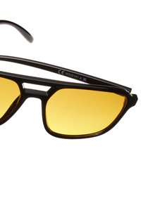 Černé sluneční brýle se žlutými čočkami, které mají geometrický design, tenký rám a malý výřez na nosníky. Číslo modelu na nožičce.