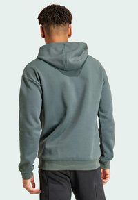 Sudadera de color verde oscuro con capucha ajustable, puños acanalados y dobladillo. Tejido suave y con textura que muestra un diseño simple y clásico.