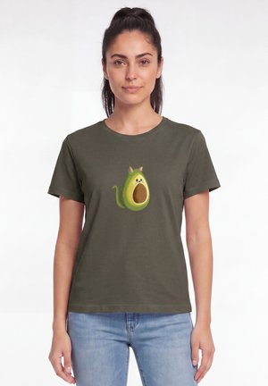 Frau trägt ein olivgrünes T-Shirt mit einer Grafik einer Avocado, die als Katze gestaltet ist, vorne, kombiniert mit hellblauen Jeans.