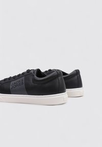 Zapatillas de cuero negro con textura suave, suelas de goma blanca y un diseño de rayas grises en el costado. Cierre con cordones.