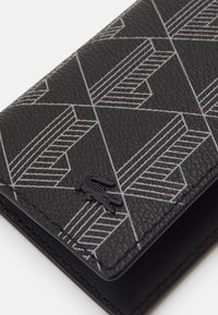 Portefeuille noir texturé arborant un motif géométrique blanc et un petit accent logo noir. Design compact avec bords arrondis.