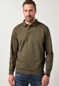 Oliwkowa, długąsleeve, polo koszula z kołnierzykiem zapinanym na guziki, prążkowane mankiety i mały akcent logo na klatce piersiowej. W połączeniu z ciemnoniebieskimi dżinsami.