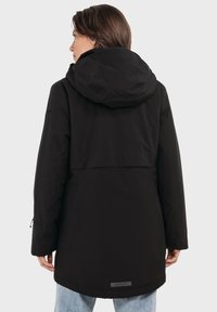 Schwarze Parkajacke mit Kapuze, lockerer Schnitt, langen Ärmeln und längerem Rückensaum. Glatte, matte Oberfläche mit minimalen Akzenten.