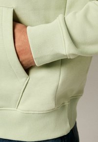 Light green sweatshirt with ribbed cuffs and hem, featuring a kangaroo pocket and smooth texture, showcasing clean lines and simple design.