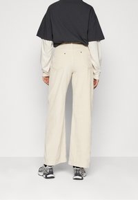 Crème-kleurige corduroy wijde broek met achterzakken, gecombineerd met een grijze T-shirt met korte mouwen en sportieve zwarte schoenen.